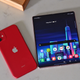 A red iPhone 11 face down next to a Samsung folding phone that lies open, with the display on. Both lie on a marble countertop.